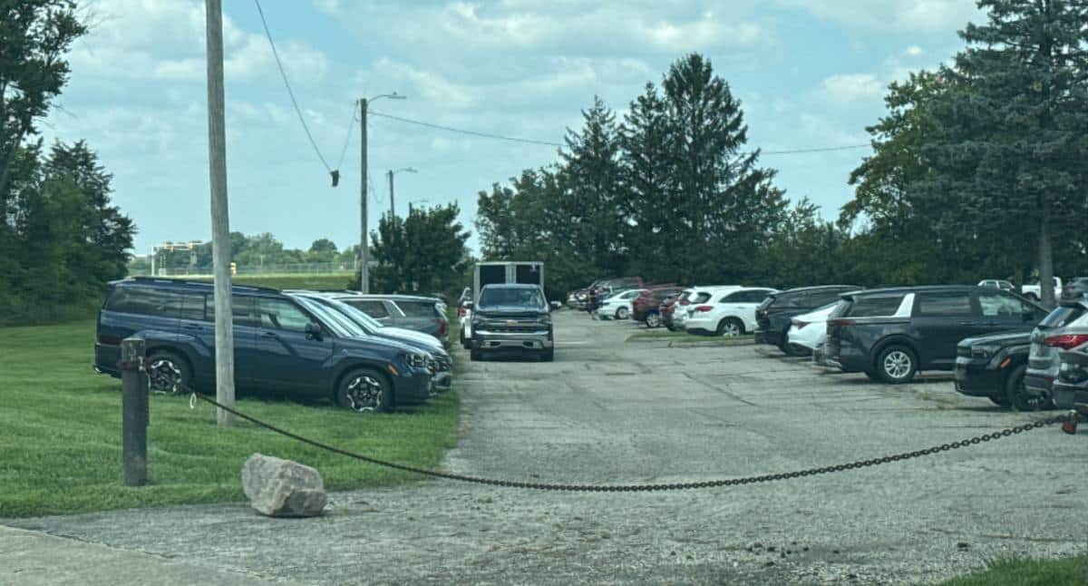 The former Airport Inn site in Vandalia, Ohio: cracked asphalt with grass through the seams, rows of new SUVs and pickups stored on it, and the entrance closed off by a chain between two posts.